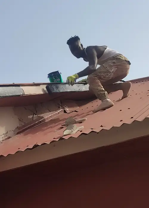 Pabi's Painting team member on top of a roof painting the fascia board during a home improvement project in The Gambia.